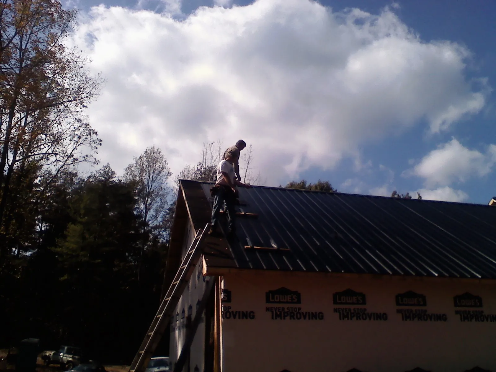 Roofer fastening dark metal panels high against a cloudy sky, from a Roof Inspection job in Clio