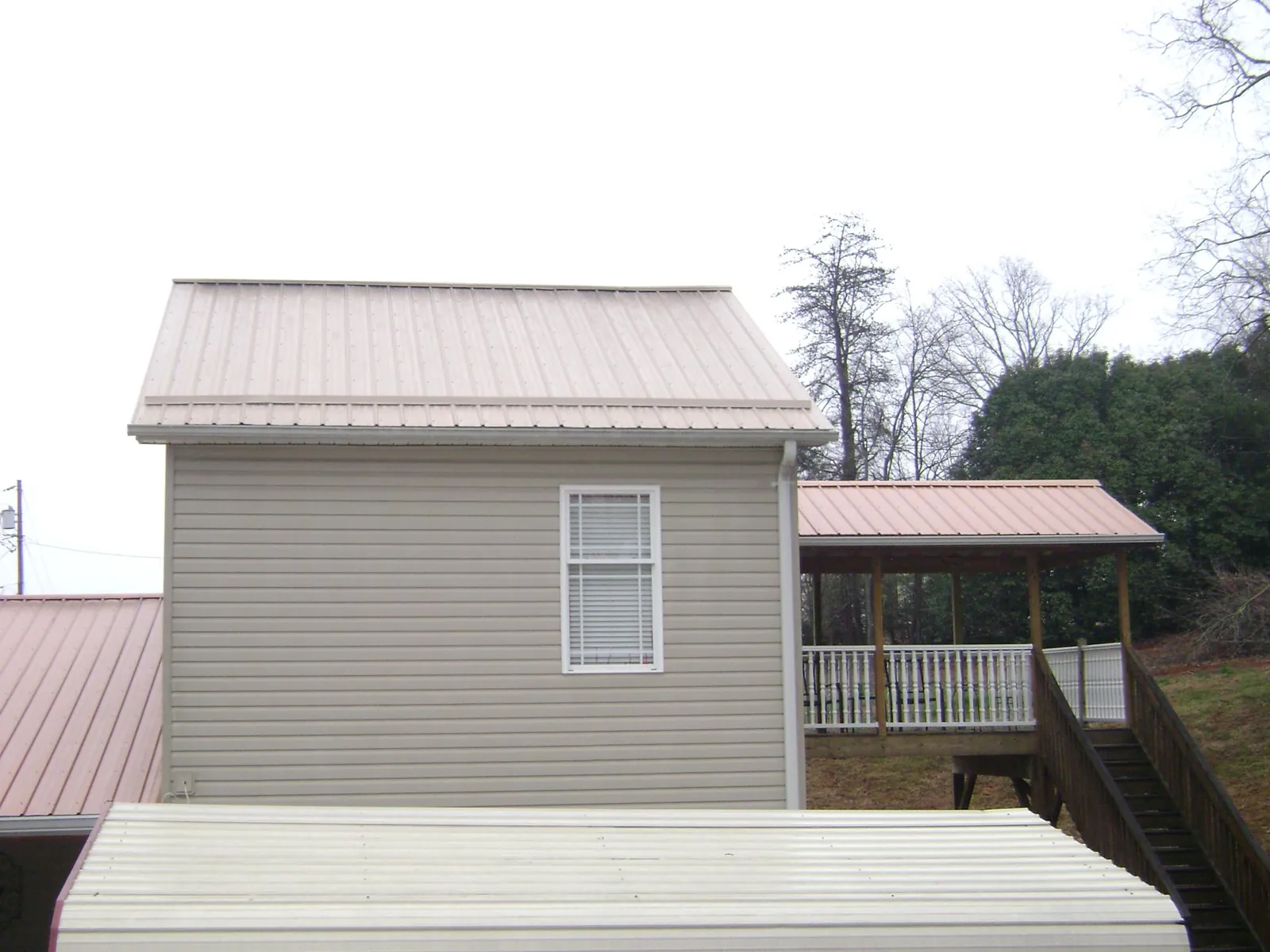 Tan metal roofs on a two story addition and attached porch, from a Roof Replacement job in Clio